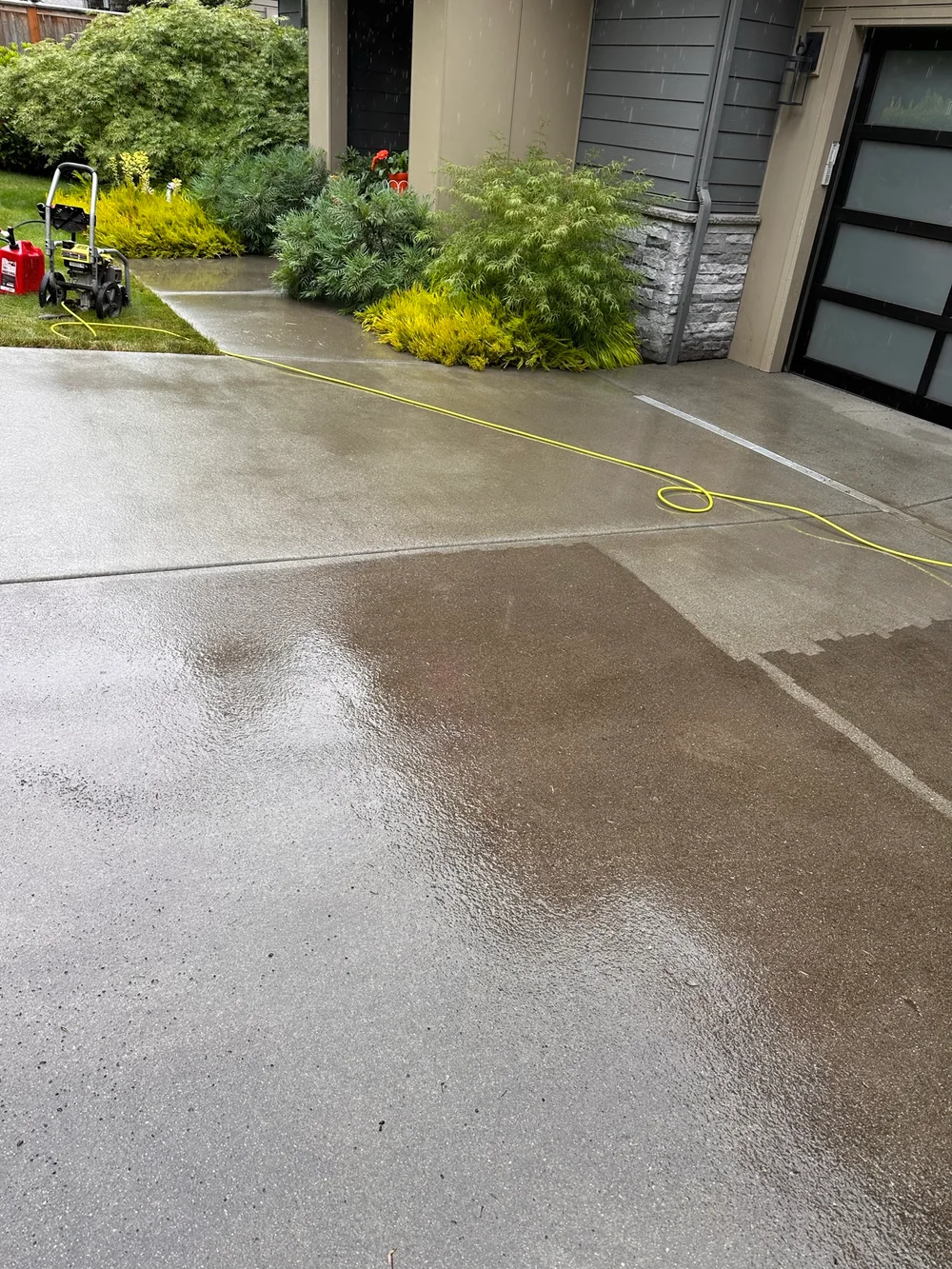 Pressure washing a concrete driveway beside a home